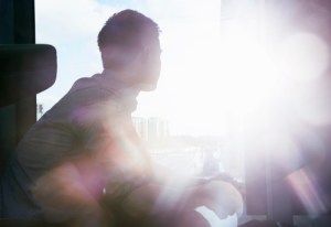 silhouette of man looking out window with flare