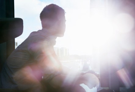 silhouette of man looking out window with flare